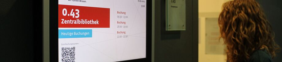Link zur Lernraumübersicht Kopf von hinten, der auf digitale Raumanzeige in der SLUB schaut