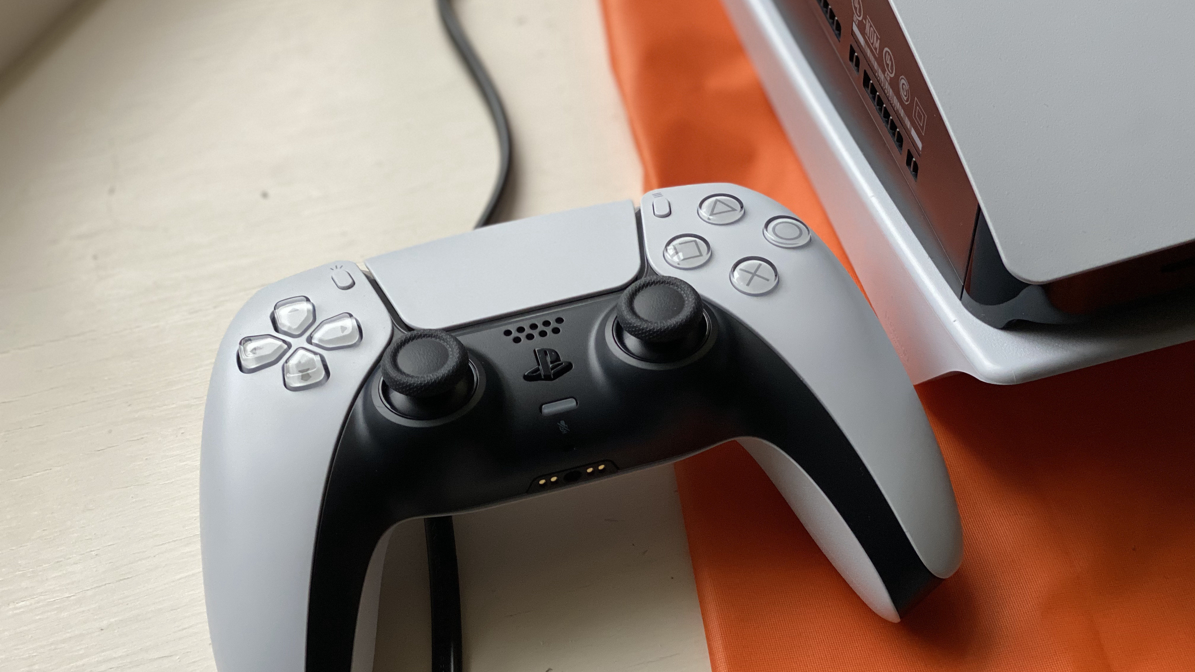 A white PS5 DualSense controller sitting on a wooden surface next to a white PS5