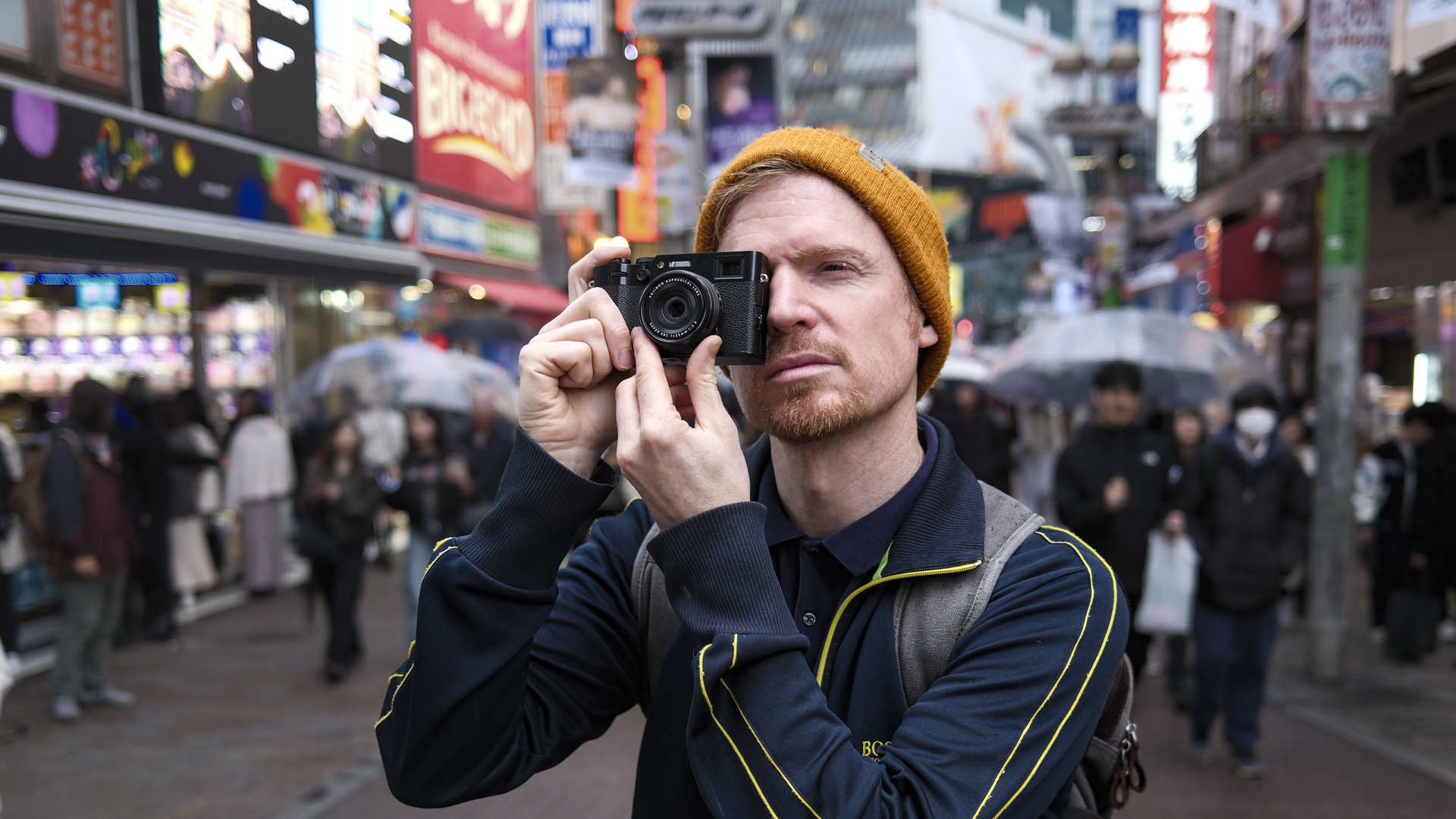 Person holding the Fujifilm X100VI camera up to their eye with a bustling Tokyo city background 