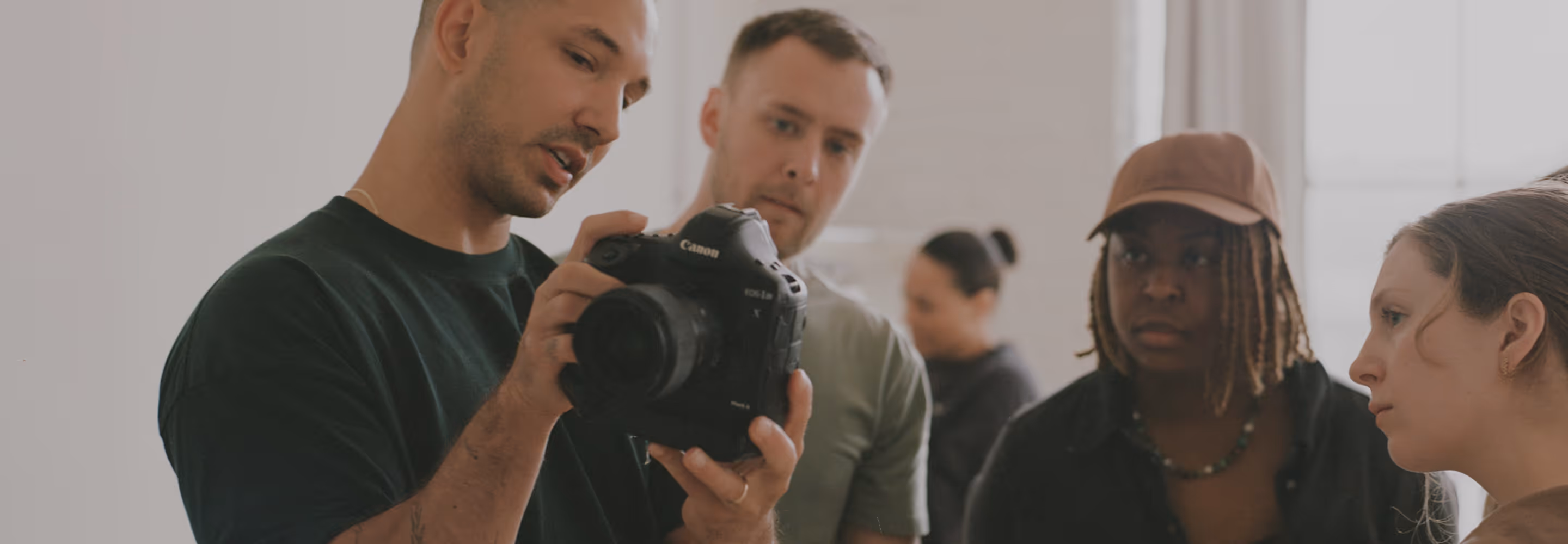 A photography coach showing a Canon camera screen to 3 members of a photography coaching program inside a softly lit room.