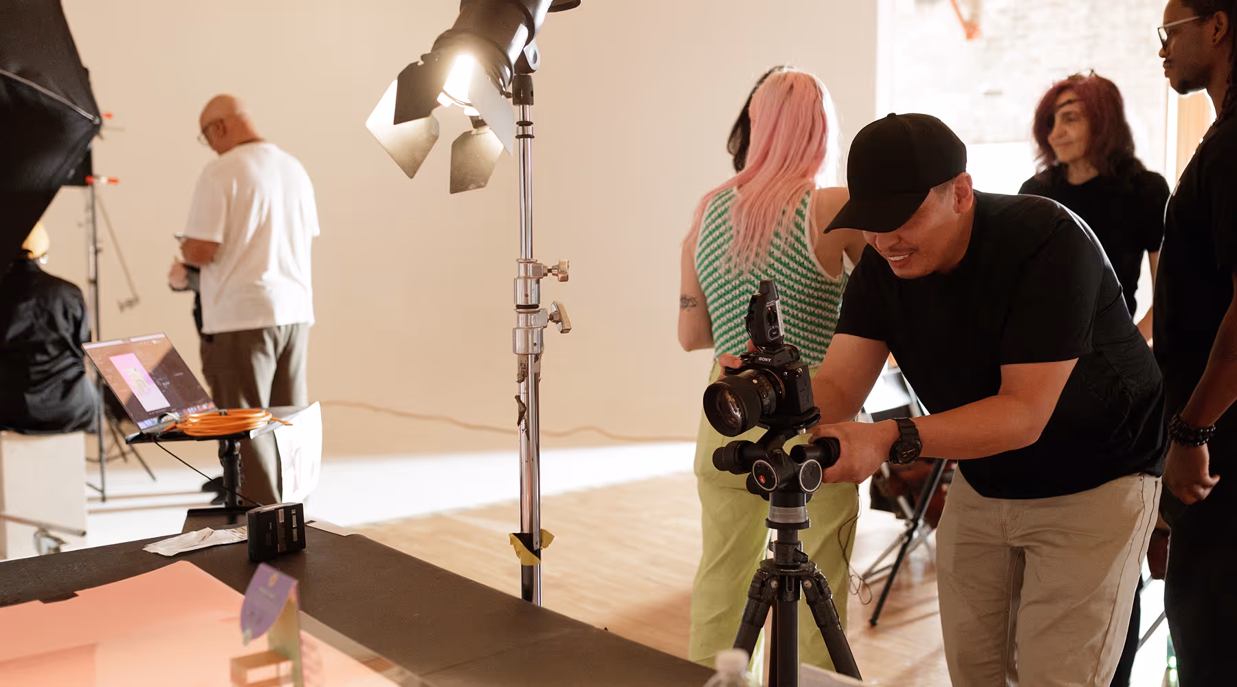 Photographer adjusting a camera on a tripod in a studio with crew members and lighting equipment in the background during a photography workshop