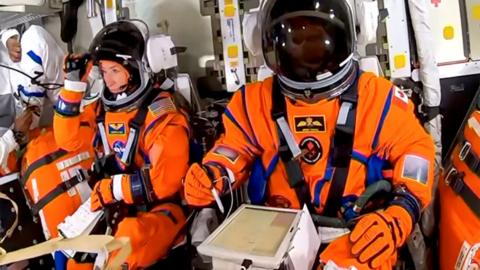 two of the crew of the artemis shown in orange spacesuits inside the spacecraft