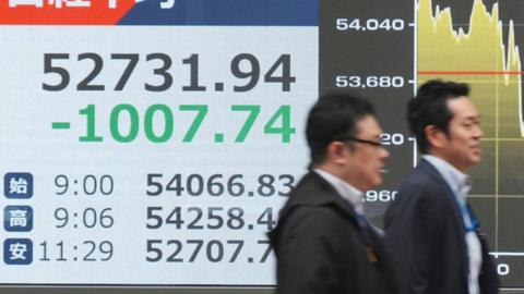 Passersby walk past electronic quotation boards displaying the Nikkei Stock Average on the Tokyo Stock Exchange