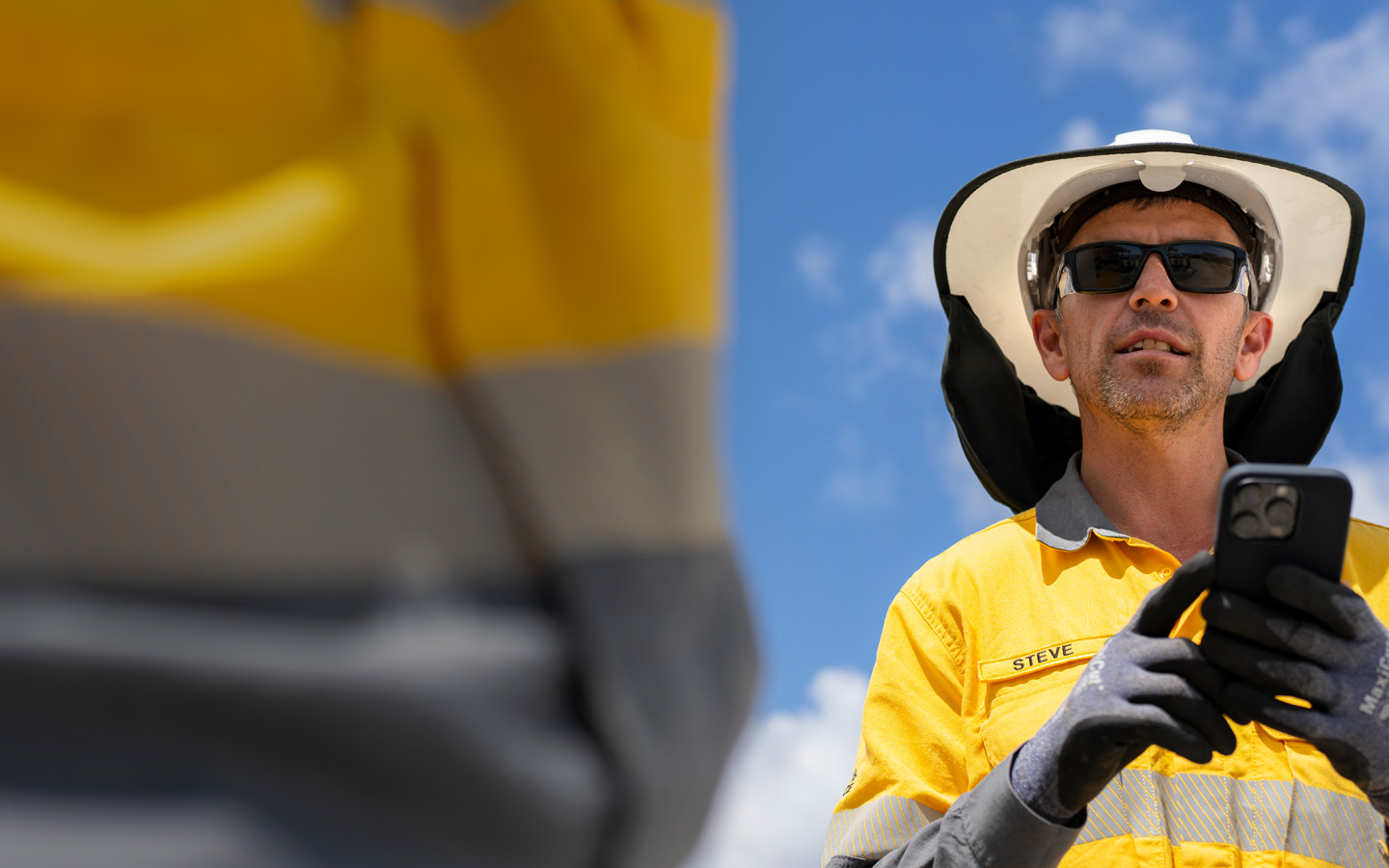 A fieldworker dressed in safety gear holds an iPhone while talking with a crew member